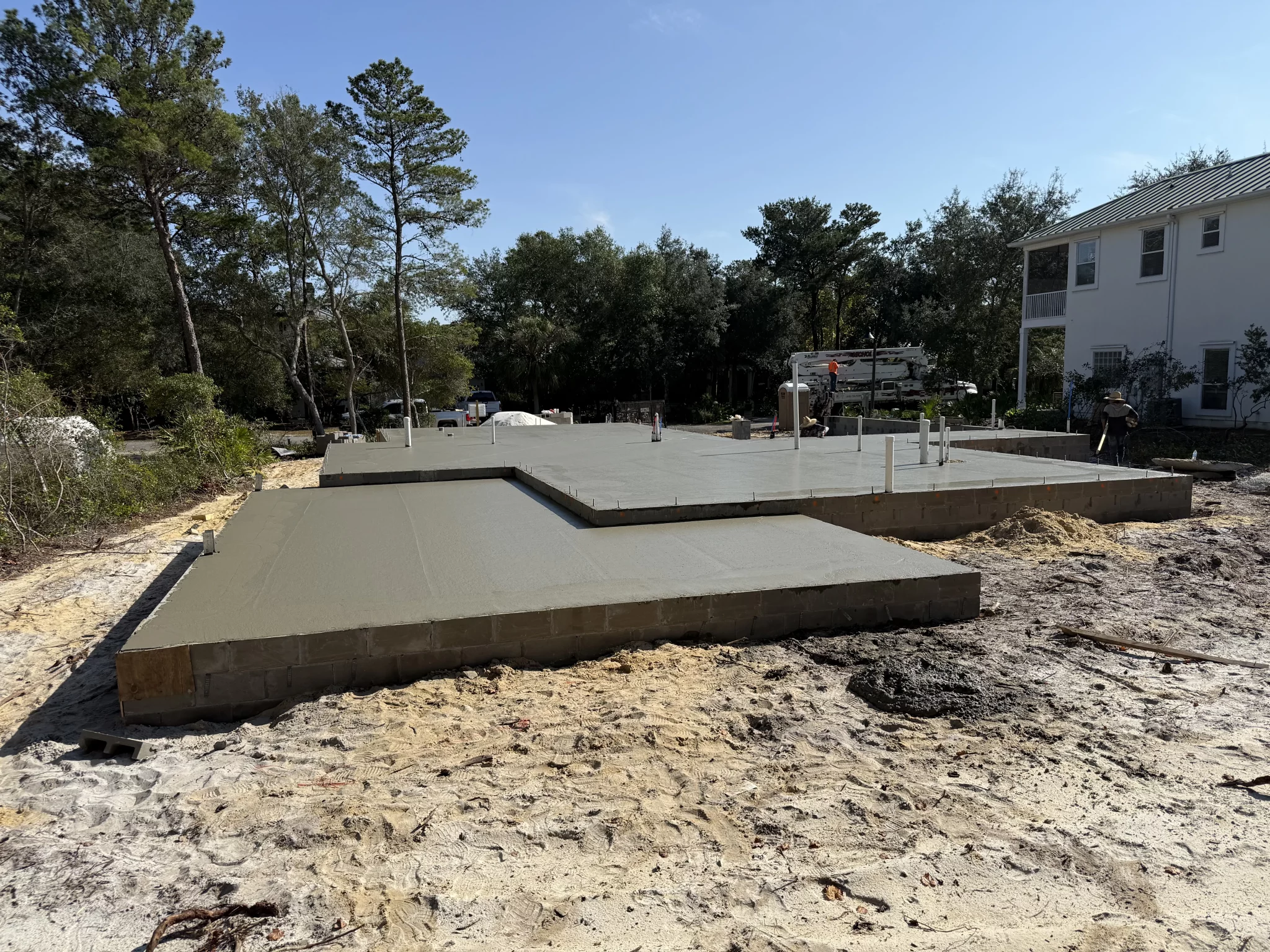 Stepped concrete slab foundation for new construction on sandy ground, with rebar and trees in the background.
